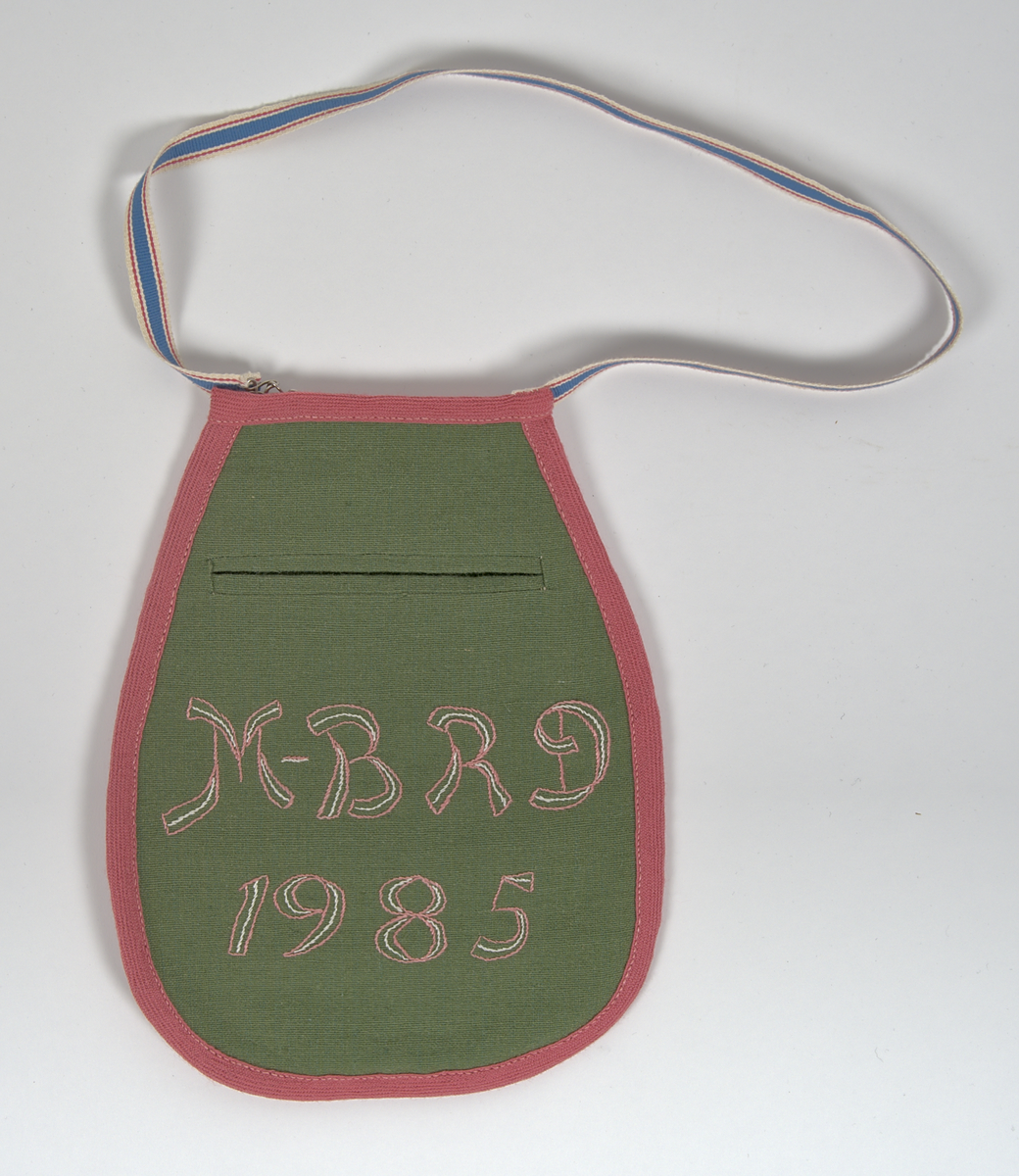 Bygdedräkt i 8 delar. 

a) Livstycke - Grönt livstycke av ylle med rosa broderier och snörning framtill.

b) Skjortlinne - Vitt skjortlinne av linne med broderier i rosa och blått. MBRD 1984.

c )Kjol - Blå handsydd kjol i ylle. Fållad med förstärkning av rödvittrutigt tyg.

d )Förkläde - Förkläde av linne. Vitt, med rosa och blåa detaljer

e) Hätta - Svart bindmössa i syntetsiden broderad med blommor i rosa, blått och gult. Nertill finns blåa och röda blommor omfamnat i ett bladverk i grönt. 

f) Sjal - Blå sjal broderad med färgrikt blommotiv.

g )Kjolväska - Grön ylleväska med rödrosa band som fåll. Broderat med M-BRD 1985. Blåvitt band för fastsättning i kjolen.

h) Kvitton - 1 st kuvert med 7st kvitton för de kostnader som dräkten gick på. Enligt givarens egna uträkningar kostade dräkten 2586kr att tillverka. Då är även kurskostnaden inräknad.

Det medföljer även fotografier på givaren iklädd dräkten och en mindre artikel om dräkten.