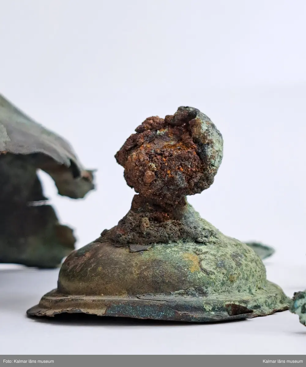 KLM 4911. Sköldbuckla, av brons. Den översta knoppen är av järn och överdragen av brons. En halvsfärisk nit. Sköldbucklan är i flera delar. Gravfynd tillsammans med KLM 4912-4915.