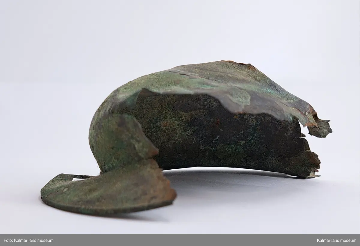 KLM 4911. Sköldbuckla, av brons. Den översta knoppen är av järn och överdragen av brons. En halvsfärisk nit. Sköldbucklan är i flera delar. Gravfynd tillsammans med KLM 4912-4915.