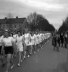 Gymnastikuppvisningen, 25/5 1941. 
En vitklädd gymnastiktrupp, bestående av kvinnliga gymnaster, marscherar fram längs Storgatan, västerut. I bakgrunden syns en av flyglarna till dåv. Växjö Stads Försörjningsinrättning, senare en del av Folkskoleseminariet (Västerled).