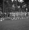 Gymnastikuppvisningen, 25/5 1941. 
Kvinnliga gymnaster tågar in på Värendsvallen. Genom skogen i 
bakgrunden skymtar några av kasernerna på I 11.