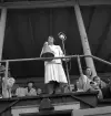 Gymnastikuppvisningen, 25/5 1941. 
En vitklädd dam i dräkt står med megafon i hand, vid mikrofonen på
läktaren till Värendsvallen.