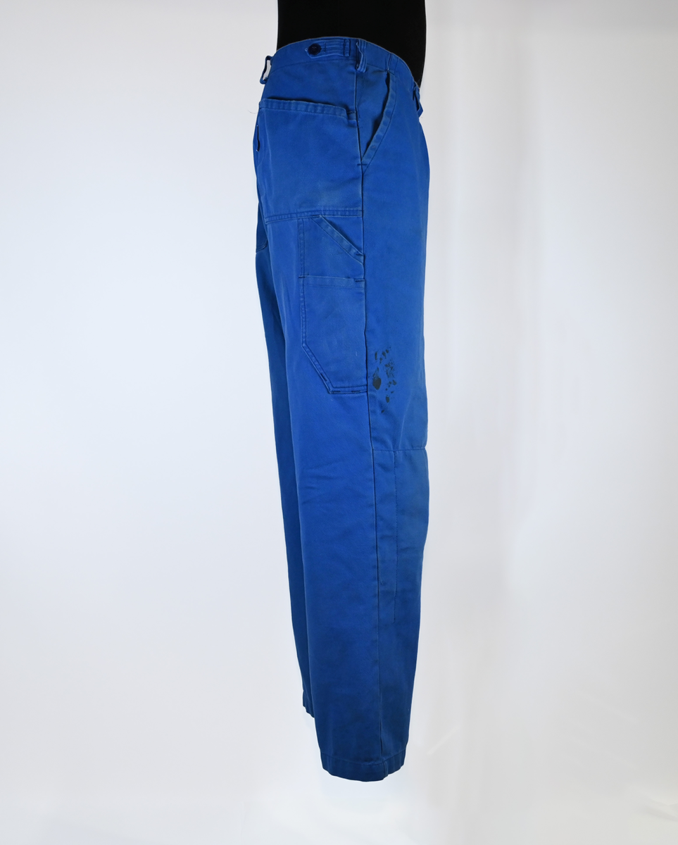 Byxa i blått tyg i modell arbetsbyxa. På båda byxbenen finns invändiga fickor för knäskydd. Sju öglor för livrem samt nio fickor varav en har lock med metallknapp. På vardera sida om byxlinningen sitter en kapp med tillhörande tygbit för att kunna reglera midjan. Storlek 58.

"Björnkläder" står skrivet på en fastsydd tygetikett på vänster bakficka. Texten är skriven i vita bokstäver och bakgrunden är blå.

"Björnkläder" står även skrivet på insidan längs med byxlinningen. Texten är skriven i mörkblåa bokstäver på blå bakgrund.

"Björnkläder / 58" står på fastsydd etikett vid inre byxlinning tillsammans med motiv av en björn. Texten är i gult på blå bakgrund.