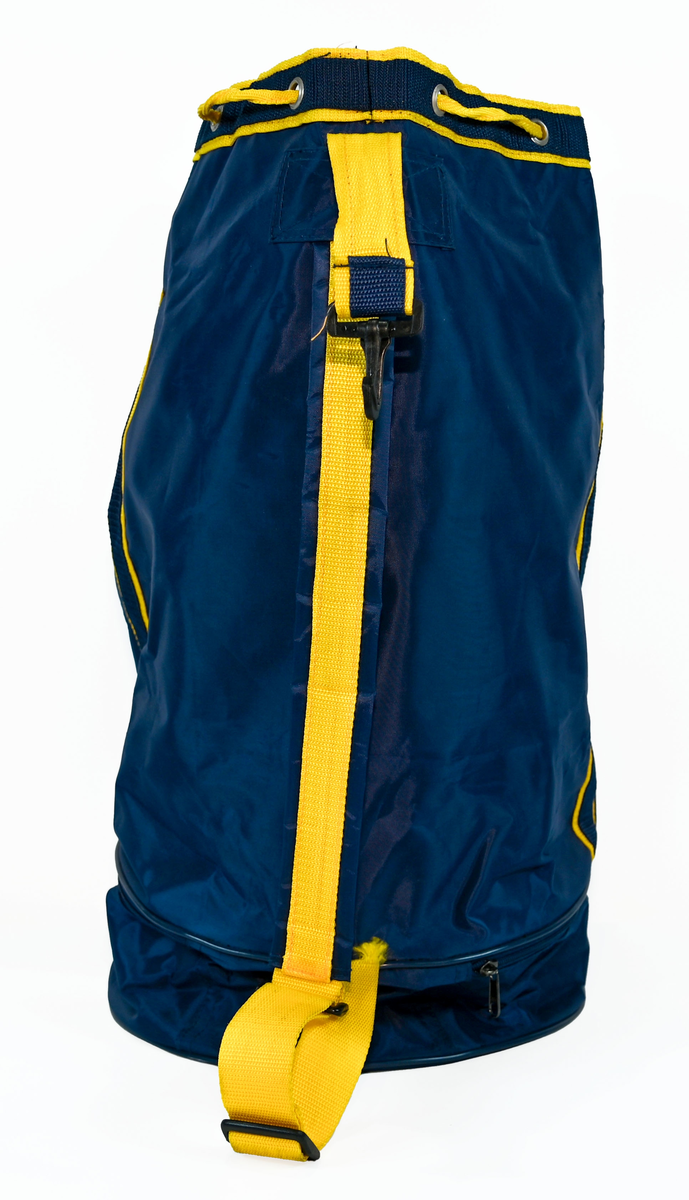 Mörkblå sjösäck med gula detaljer. På väskan står 'TRANSWEDE' och ett avbildat flygplan. Öppningen sitter upptill och går att stänga med ett gult rep samt en hake. Väskan går även att öppna från sidan genom en dragkedja. Det finns två fickor, en framtill samt en vid botten, båda med dragkedja.