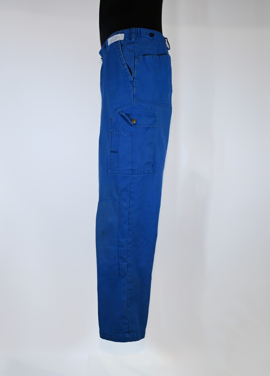 Byxa i blått tyg i modell arbetsbyxa. På båda byxbenen finns invändiga fickor för knäskydd. Sju öglor för livrem samt nio fickor varav en har lock med metallknapp. På vardera sida om byxlinningen sitter en kapp med tillhörande tygbit för att kunna reglera midjan. Storlek 58.

"Björnkläder" står skrivet på en fastsydd tygetikett på vänster bakficka. Texten är skriven i vita bokstäver och bakgrunden är blå.

"Björnkläder" står även skrivet på insidan längs med byxlinningen. Texten är skriven i mörkblåa bokstäver på blå bakgrund.

"Björnkläder / 58" står på fastsydd etikett vid inre byxlinning tillsammans med motiv av en björn. Texten är i gult på blå bakgrund.