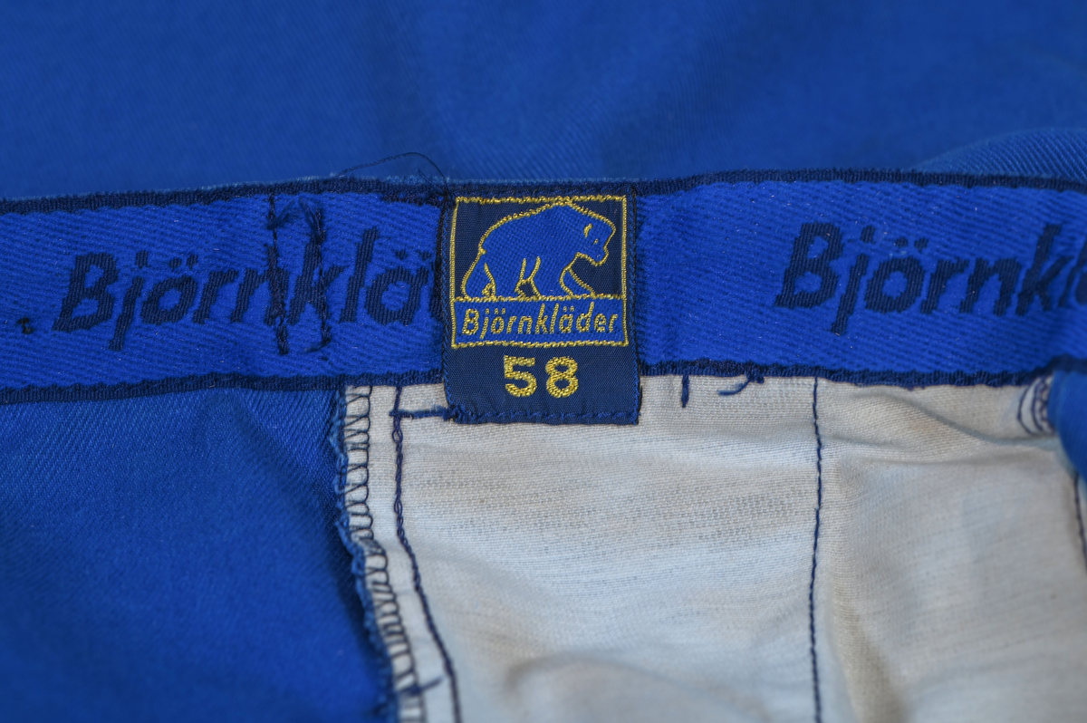 Byxa i blått tyg i modell arbetsbyxa. På båda byxbenen finns invändiga fickor för knäskydd. Sju öglor för livrem samt nio fickor varav en har lock med metallknapp. På vardera sida om byxlinningen sitter en kapp med tillhörande tygbit för att kunna reglera midjan. Storlek 58.

"Björnkläder" står skrivet på en fastsydd tygetikett på vänster bakficka. Texten är skriven i vita bokstäver och bakgrunden är blå.

"Björnkläder" står även skrivet på insidan längs med byxlinningen. Texten är skriven i mörkblåa bokstäver på blå bakgrund.

"Björnkläder / 58" står på fastsydd etikett vid inre byxlinning tillsammans med motiv av en björn. Texten är i gult på blå bakgrund.