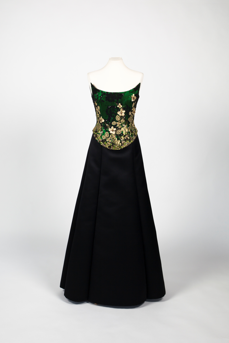 Småblomster og blader som vokser opp av en blomstereng, alt av gull, mot en bakgrunn av storblomstret tyllblonde.