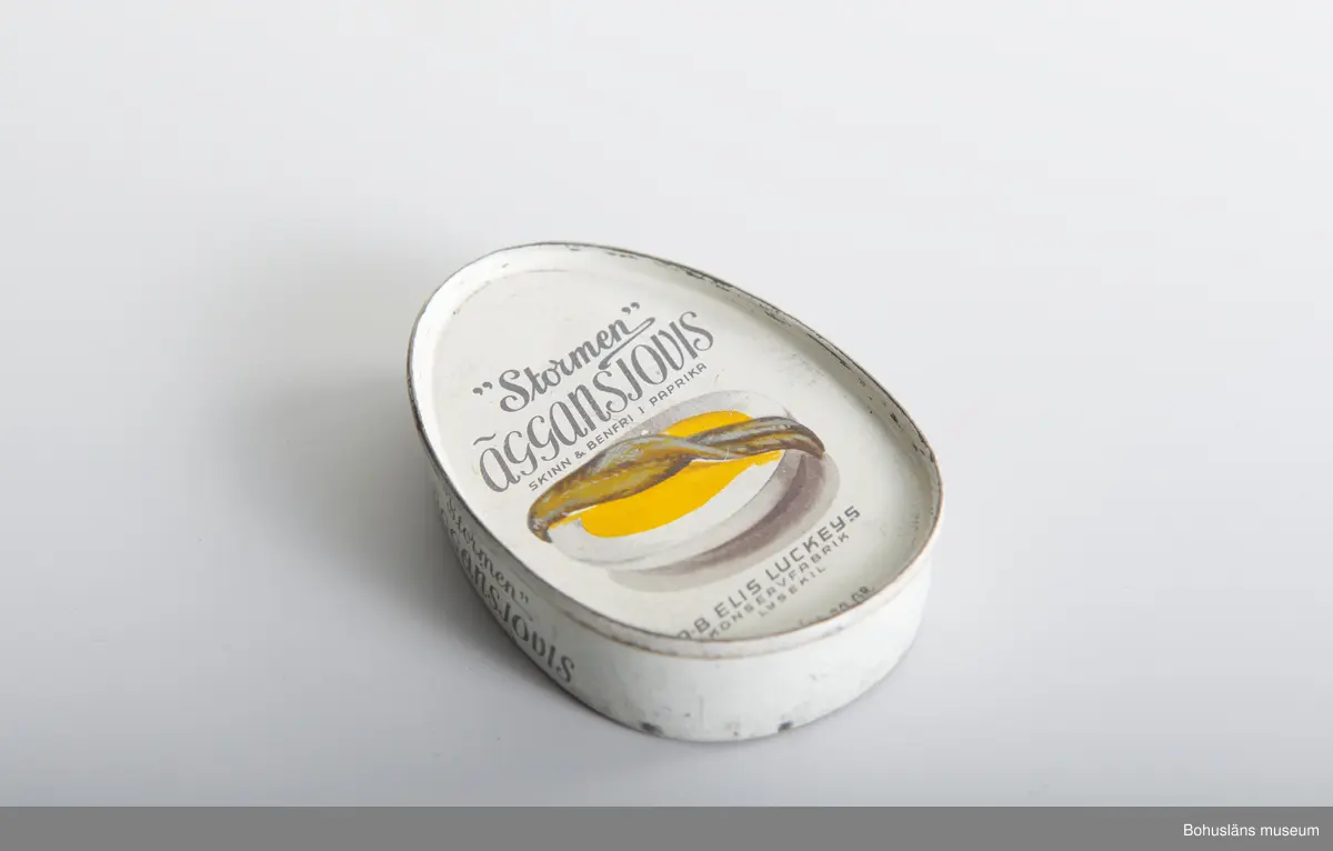 Närmast oval burk, dekor tryckt direkt på plåten i vitt och svart samt bild av ansjovis och äggskiva Text:" "Stormen" Äggansjovis skinn & benfri AB Elis Luckeys konservfabrik Samma bild och och text på baksidan.
Om givaren se UM026667