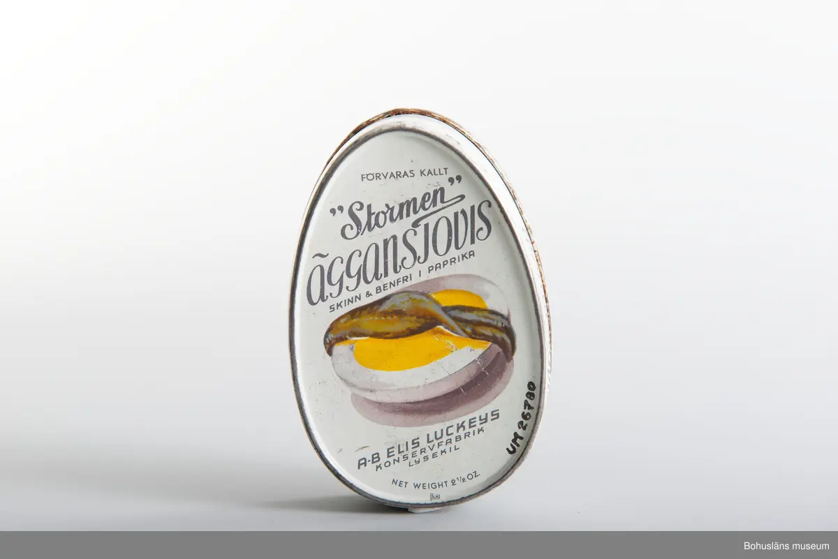 Närmast oval burk, dekor tryckt direkt på plåten i vitt och svart samt bild av ansjovis och äggskiva Text:" "Stormen" Äggansjovis skinn & benfri AB Elis Luckeys konservfabrik Samma bild och och text på baksidan.
Om givaren se UM026667