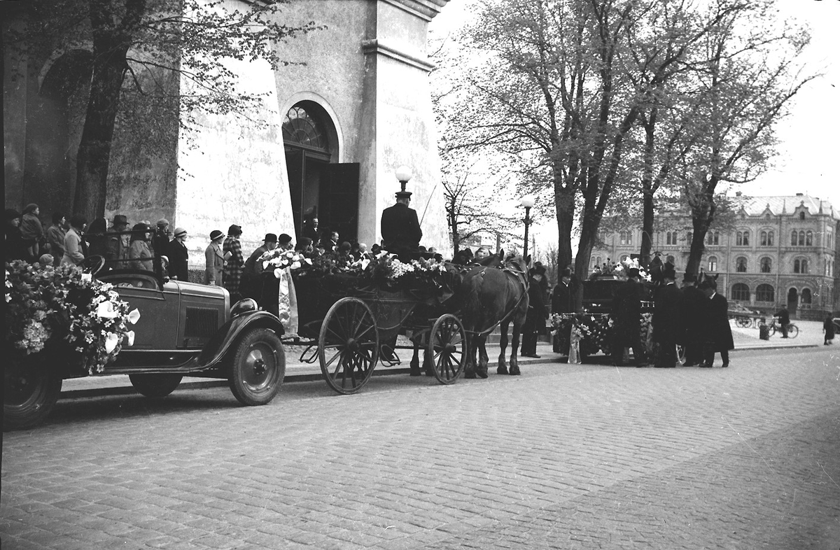 Begravningsprocession med bilar och hästar utanför Varbergs kyrka. Gatuvy från Kungsgatan. Bild 1: Hästekipage med kistan täckt av vita liljor. Kusken kan vara Alvar på Träslövsvägen som med sina hästar brukade köra vid begravningar. I förgrunden ses en prestaver. Sett från söder. Bild 2: De sörjande kommer ut från kyrkan och går mot likbilen till höger. Bild 3: Processionen sedd från norr med två hästekipage och en öppen bil.
