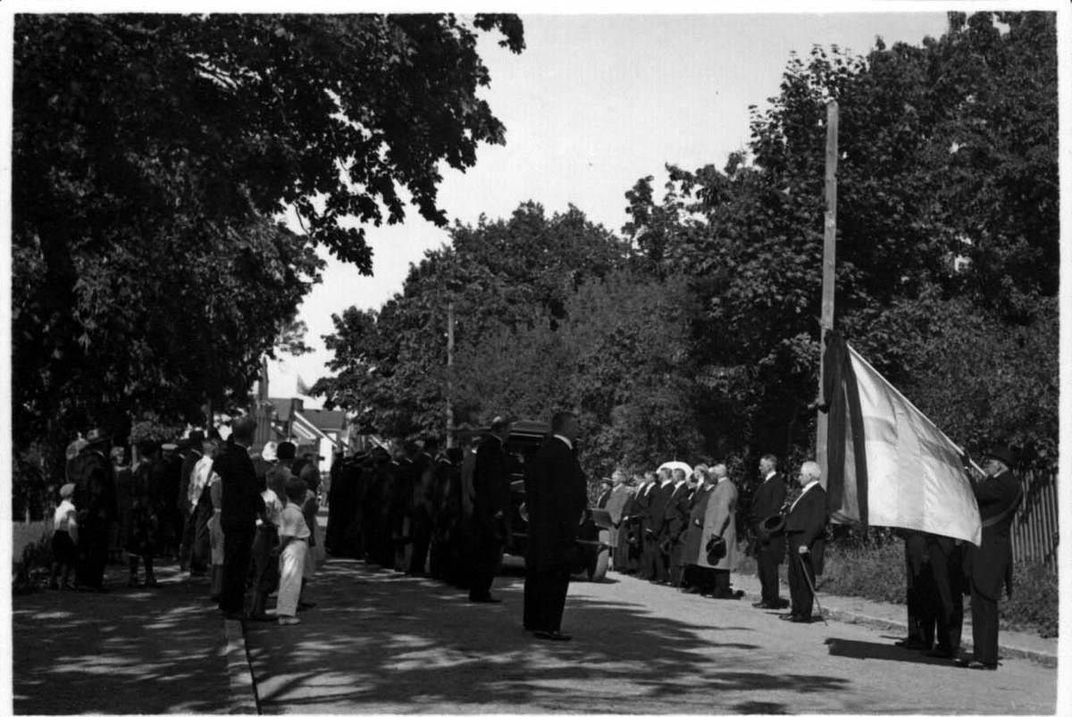 Likbilen med borgmästare Gustaf Lindgren har just passerat Söder tull i Gränna på väg söderut. Dess väg kantas närmast av mörkklädda män och kvinnor. Viktor Fong bär ett standar med flagga och sorgband.