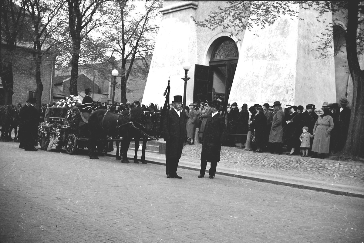 Begravningsprocession med bilar och hästar utanför Varbergs kyrka. Gatuvy från Kungsgatan. Bild 1: Hästekipage med kistan täckt av vita liljor. Kusken kan vara Alvar på Träslövsvägen som med sina hästar brukade köra vid begravningar. I förgrunden ses en prestaver. Sett från söder. Bild 2: De sörjande kommer ut från kyrkan och går mot likbilen till höger. Bild 3: Processionen sedd från norr med två hästekipage och en öppen bil.