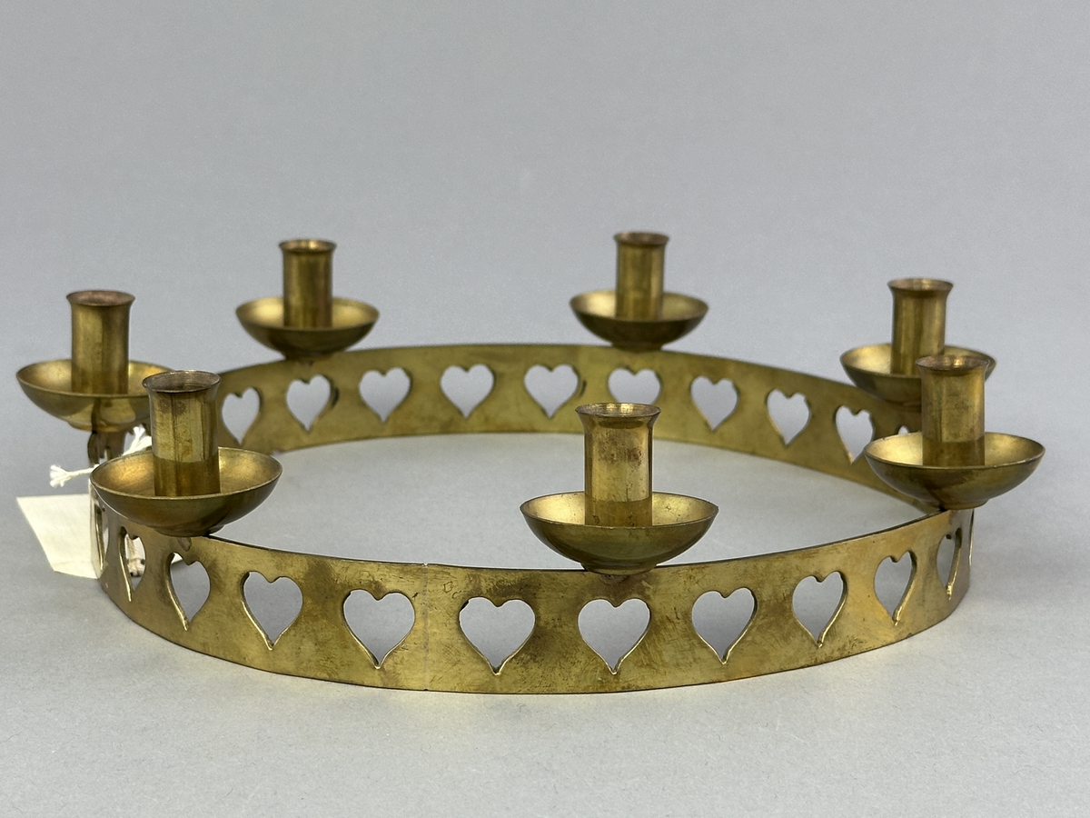 Ljusstake, "Ljusring" för sju ljus, gjord av mässingband med utstansat hjärtmönster. Ljushållarna är fastlödda på bandets högkant.