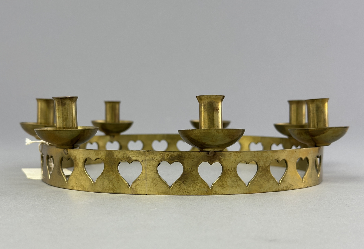 Ljusstake, "Ljusring" för sju ljus, gjord av mässingband med utstansat hjärtmönster. Ljushållarna är fastlödda på bandets högkant.
