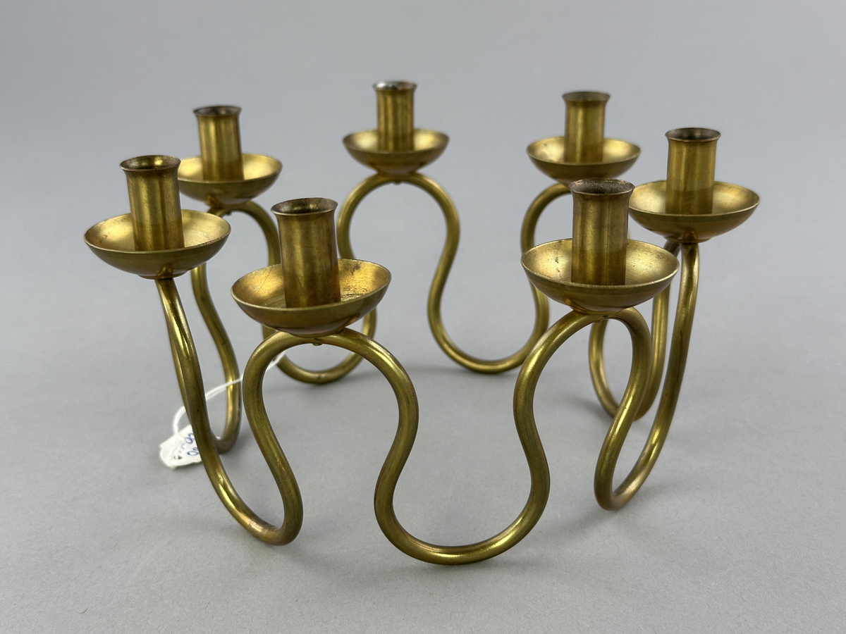 Ljusstake, "Luciakrona" för sju små stearinljus, gjord av mässingtråd som böjts i mjuk vågform. Högst upp på varje böj sitter en ljushållare fastnitad.