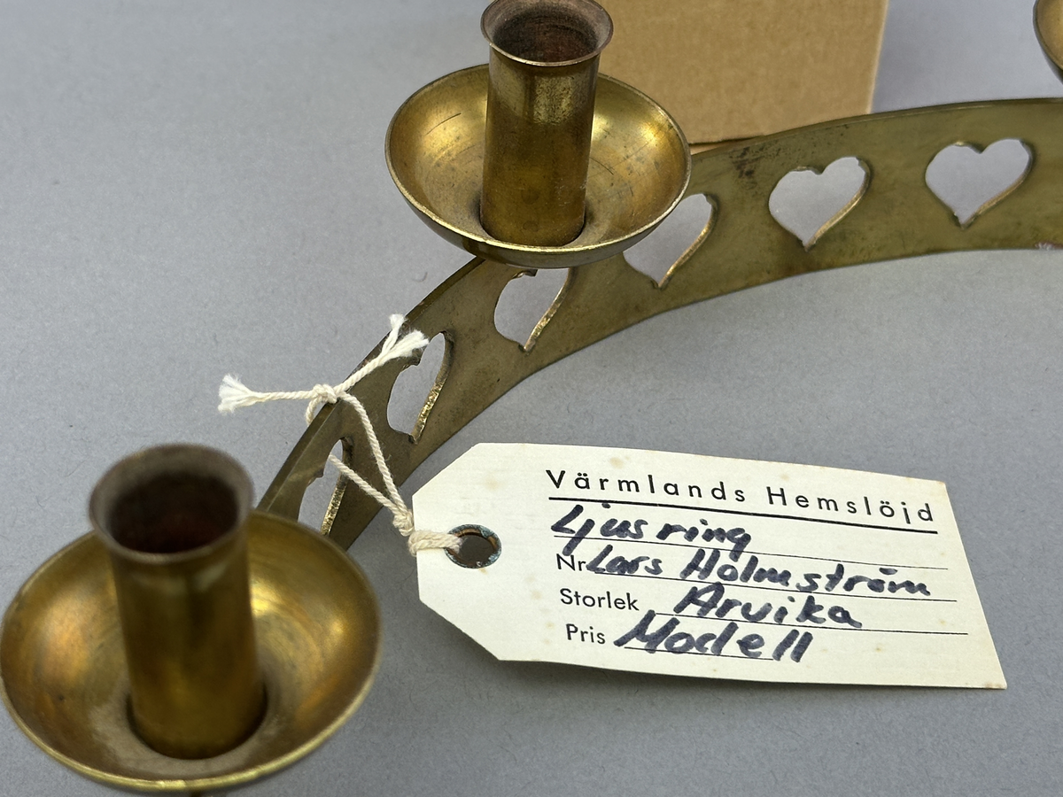 Ljusstake, "Ljusring" för sju ljus, gjord av mässingband med utstansat hjärtmönster. Ljushållarna är fastlödda på bandets högkant.