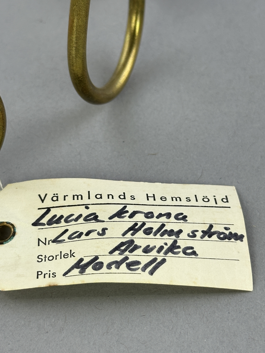 Ljusstake, "Luciakrona" för sju små stearinljus, gjord av mässingtråd som böjts i mjuk vågform. Högst upp på varje böj sitter en ljushållare fastnitad.
