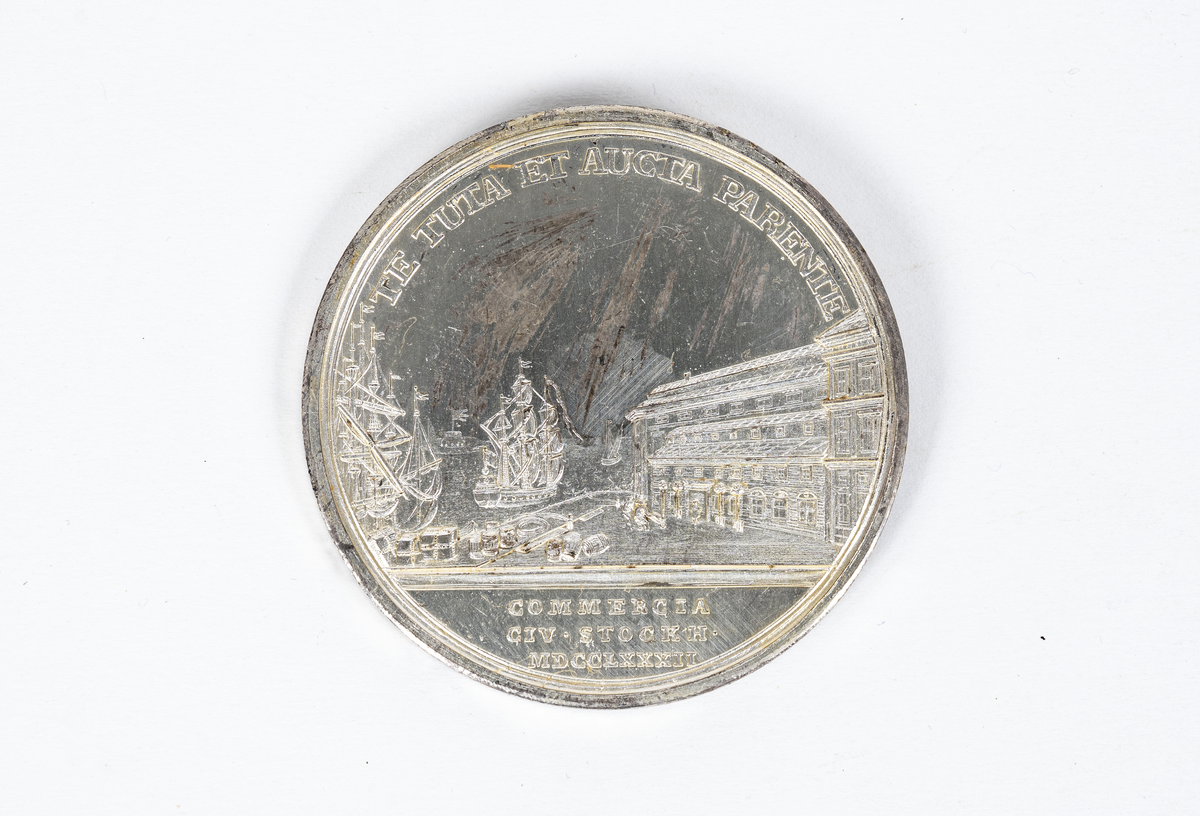 Stockholms skeppsbro, på vilken ligger tåg, packbalar och fastager och varifrån varor föras till packhoset. PÅ sjön ses fartyg, dels vid bron, dels längre ut under tillsatta segel. På avstånd ses kastellet