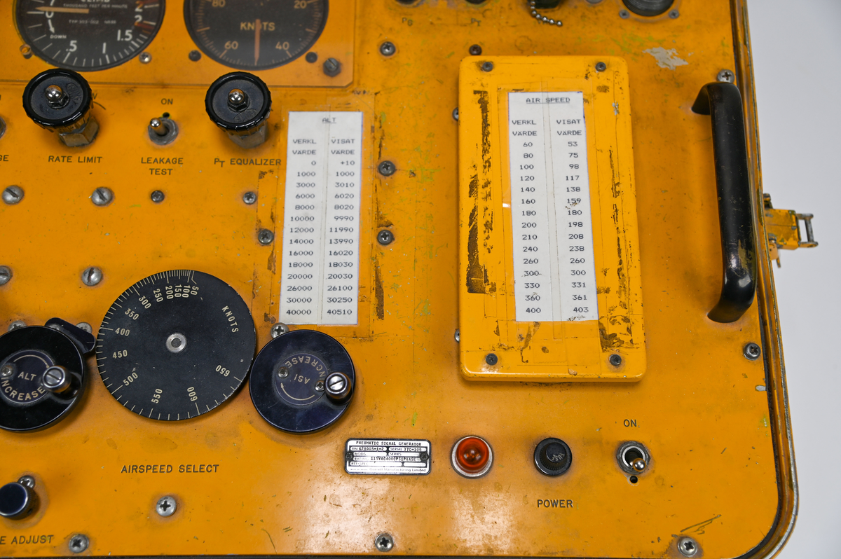 Gul plåtlåda med lock på gångjärn. Under locket en panel med 5 rattar och 3 inglasade mätare och 2 vevar. Anslutnings uttag där slangar ska skruvas fast i maskinen. Påskrift på utsidan: ”Garrett Manufacturin limited” ”Made in Canada”, i locket finns en fasttejpad kopia av en text med rubriken: ”Warning! This machine is subject to brakedownes during periods of crititcal need”, texten är ett skämt och uppmanar observatören att ”keep cool and say nice things to the machine”.