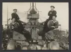 Fyra sjömän från pansarskepp Sverige tar ett humorfull gruppkort på kanonerna. Två av männen har krupit in i piporna och leker mänsklig kanonkula.
