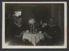 Två sjömän sitter i en vardagsrum runt ett bord med kaffekanna, porslin och en tobakspipa.