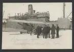 Bilden visar ett tykt flygplan typ Albatros C III. på isen framför Åland. En grupp sjömän talar med piloterna medan två andra arbetar med flygplanen. I bakgrunden syns en transportångare.