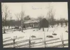 Bilden visar en enkel ladugårdsbyggnad med inhägnad i en snötäckt vinterlandskap på Åland.