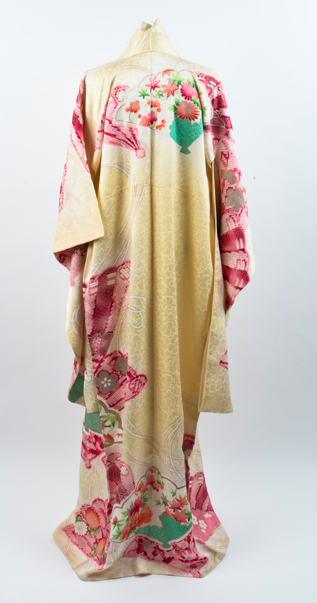 Kimono i gul silke med innvevde peoner og mønster med blomster og blader i rødt, rosa, grønt, sjøgrønt, gull og sølv. Kimonoen er fôret med kremfarget silke, nederste del er farget rosa slik at det er en jevn overgang fra rosa til kremfarget.