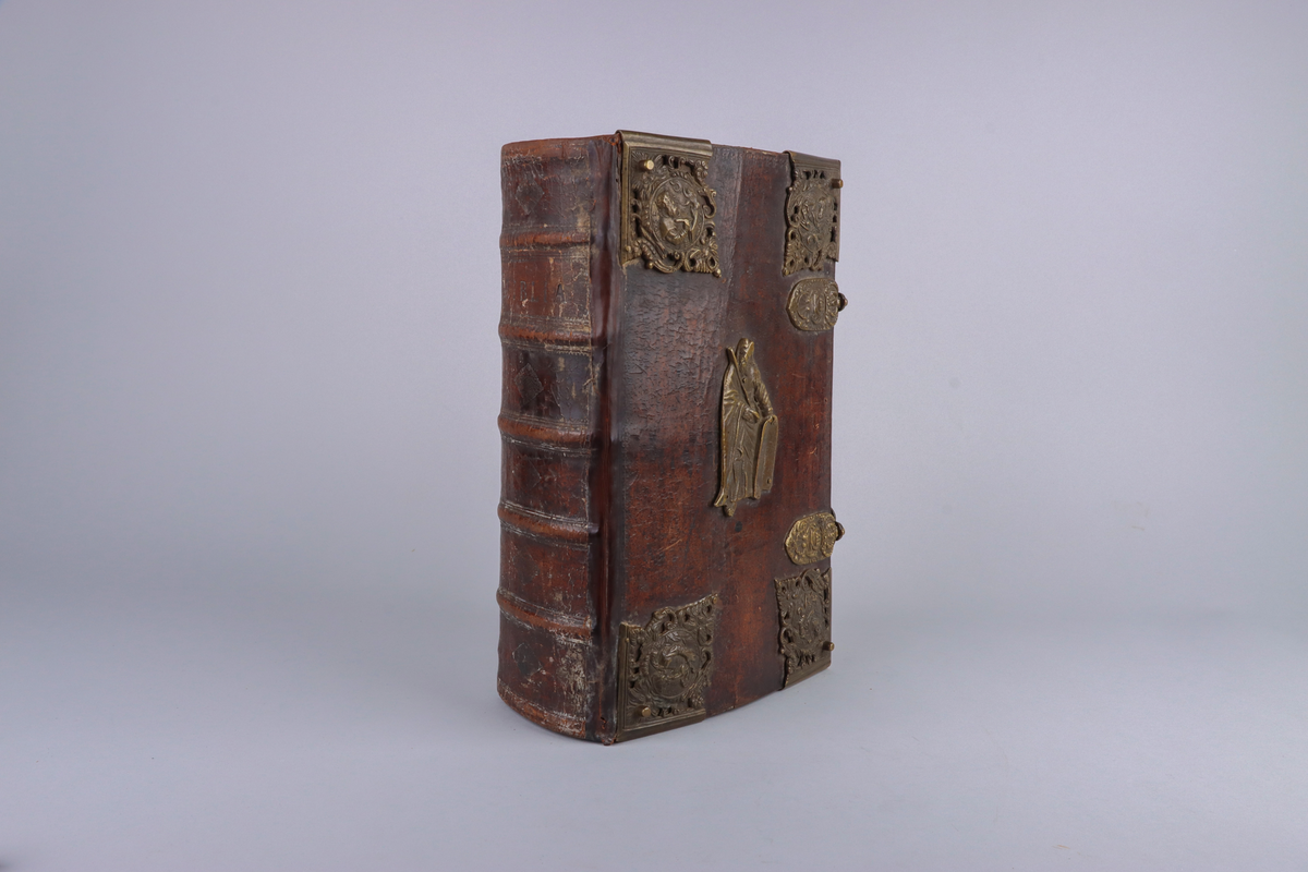 Bibel, marmorerat skinnband med upphöjda bind, dekorerad rygg. På framsida beslag i genombruten mässing med olika apostlar mitt på Moses med stentavlor. Omtag och lås med Karl XII monogram. Bibeln rymmer flertalet planscher och porträtt samt utvik med kartor.