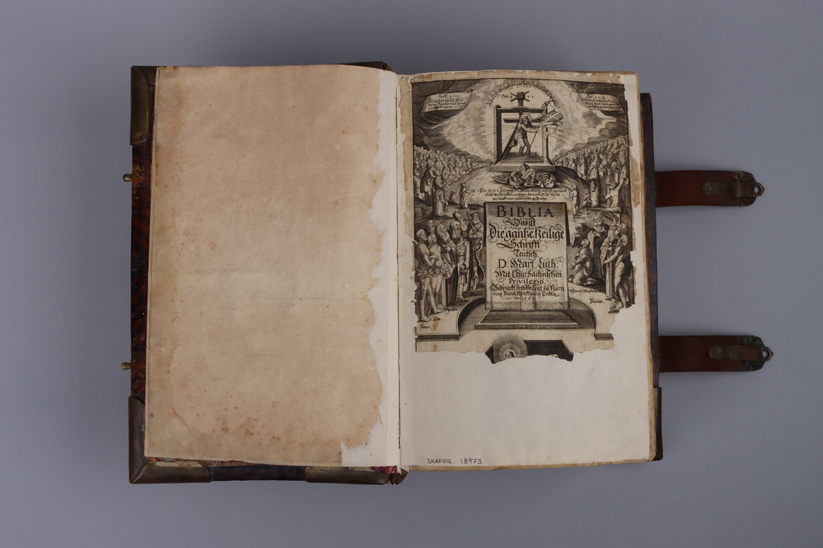 Bibel, marmorerat skinnband med upphöjda bind, dekorerad rygg. På framsida beslag i genombruten mässing med olika apostlar mitt på Moses med stentavlor. Omtag och lås med Karl XII monogram. Bibeln rymmer flertalet planscher och porträtt samt utvik med kartor.
