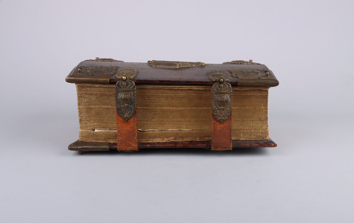 Bibel, marmorerat skinnband med upphöjda bind, dekorerad rygg. På framsida beslag i genombruten mässing med olika apostlar mitt på Moses med stentavlor. Omtag och lås med Karl XII monogram. Bibeln rymmer flertalet planscher och porträtt samt utvik med kartor.