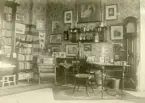 Fotot visar ett rum med bl.a , skrivbord, bokhyllor, golvur, tavlor  mm. troligen biblioteket inifrån Gysinge herrgård.