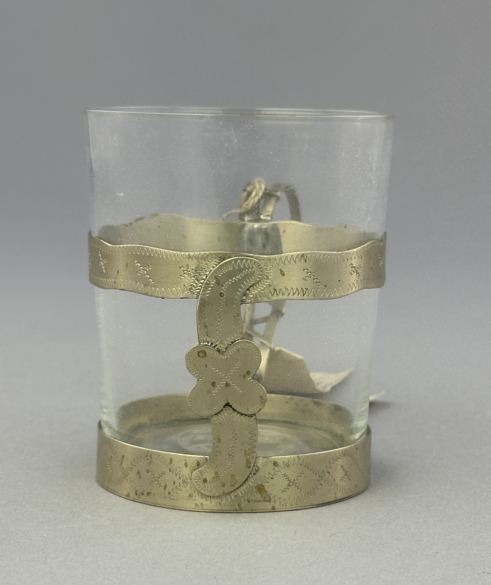 Temugg av glas och tenn. Tennhållaren är dekorerad med ristat mönster.