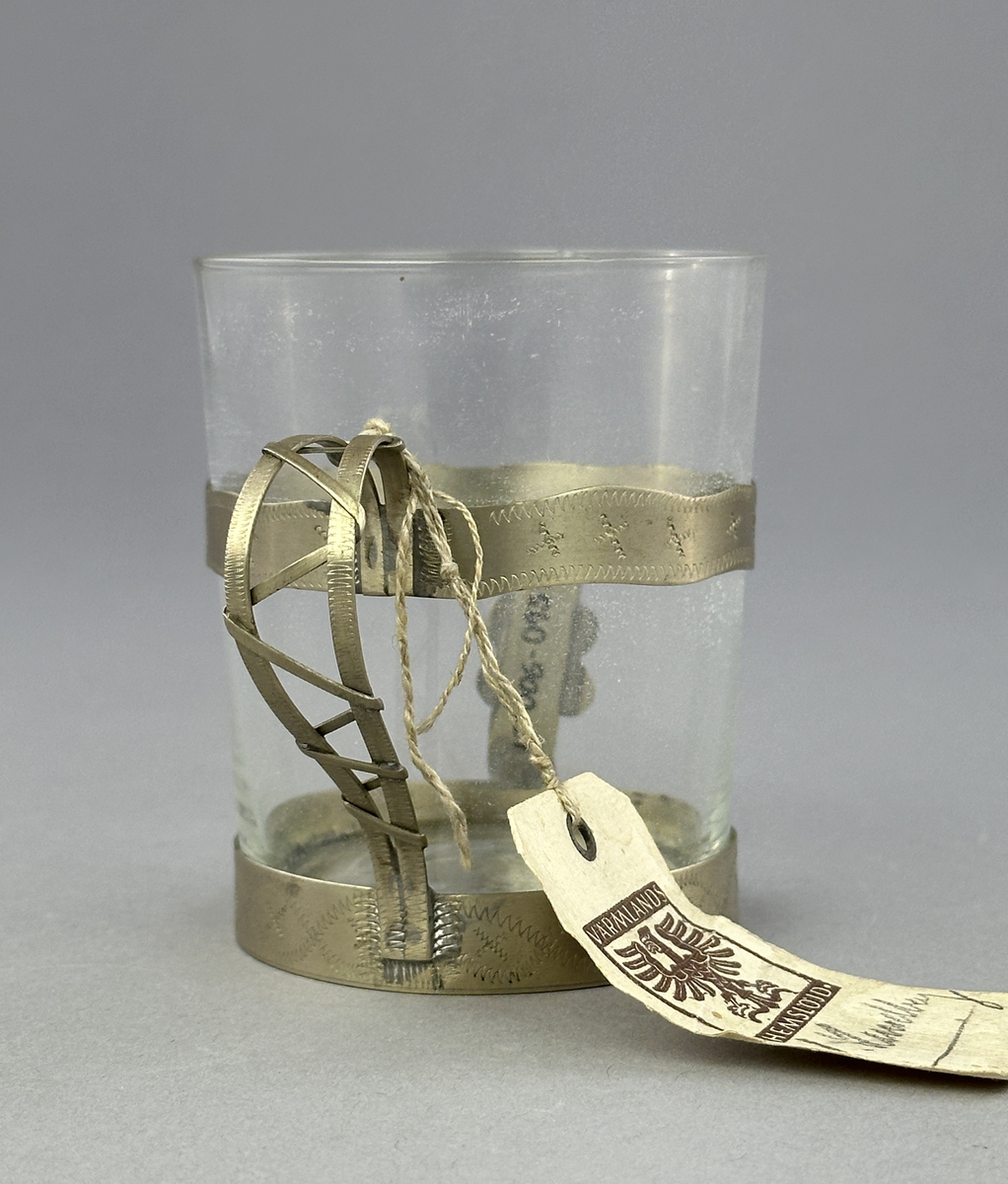 Temugg av glas och tenn. Tennhållaren är dekorerad med ristat mönster.