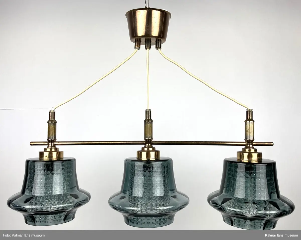 KLM 45619:387. Lampa, taklampa. Mässingstativ med tre hållare med glaskupor. De inre kuporna av genomskinligt glas med rutmönsterverkan. De yttre glaskuporna i gröngrå nyans med något som liknar ett brätte nedtill. Vit plastsladd med mässingkupa för att dölja kontakt.