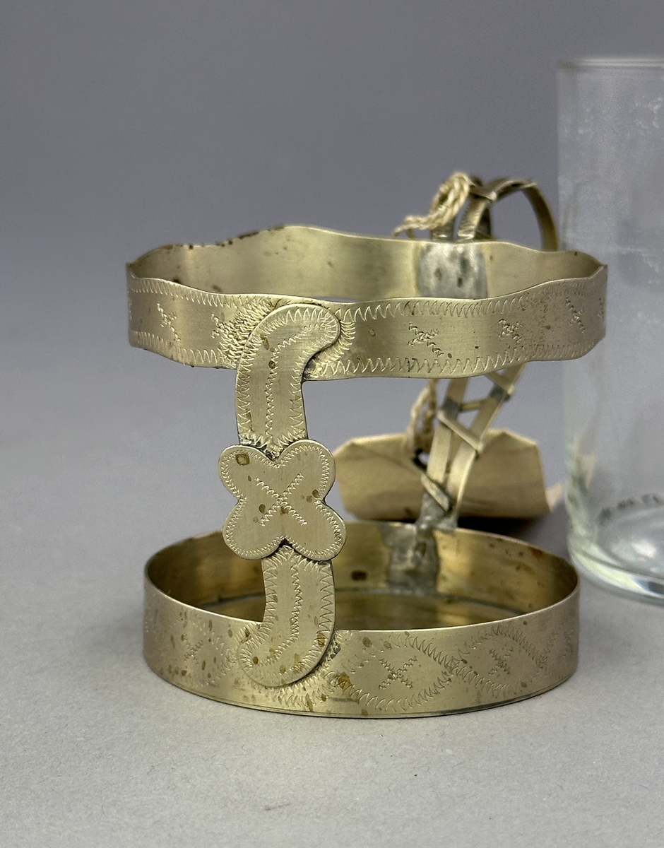 Temugg av glas och tenn. Tennhållaren är dekorerad med ristat mönster.