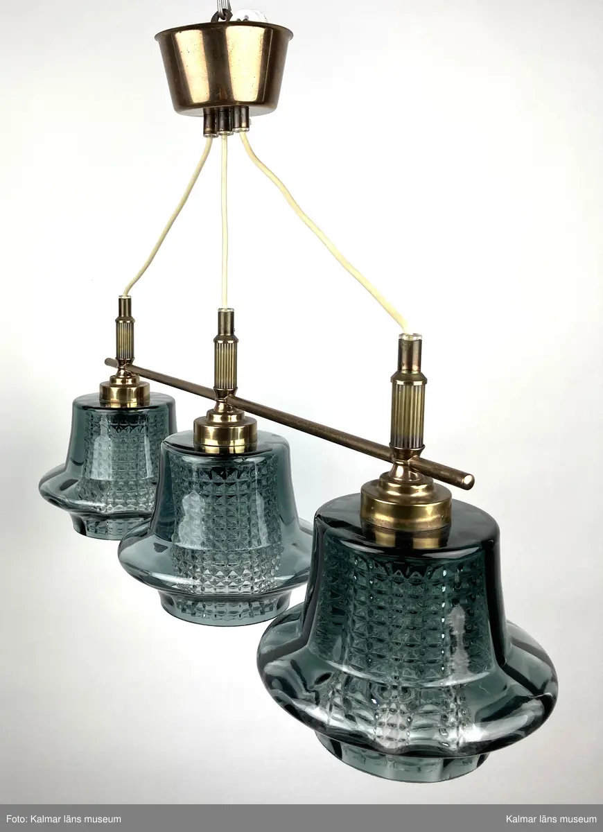 KLM 45619:387. Lampa, taklampa. Mässingstativ med tre hållare med glaskupor. De inre kuporna av genomskinligt glas med rutmönsterverkan. De yttre glaskuporna i gröngrå nyans med något som liknar ett brätte nedtill. Vit plastsladd med mässingkupa för att dölja kontakt.