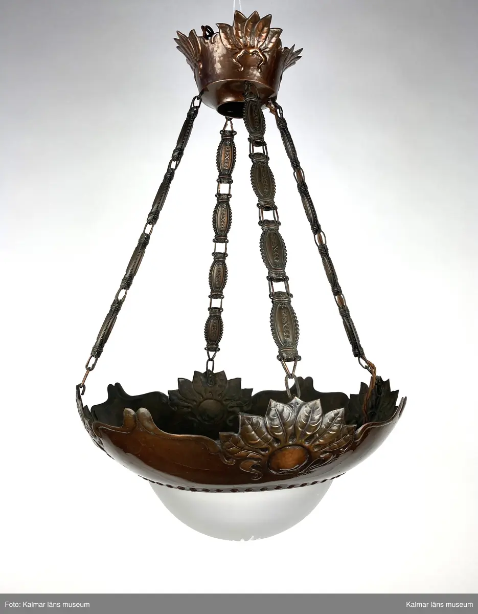 KLM 45619:396. Lampa, taklampa. Av metall med frostad vit glaskupa liggande på metallstommen. Glaskupan har slipat mönster från centrum likt en stjärna. Fyra kedjor som utgörs av avlånga metalldetaljer. Sockel för en glödlampa vid sidan av stommen samt överst i metallkupan upp mot taket.