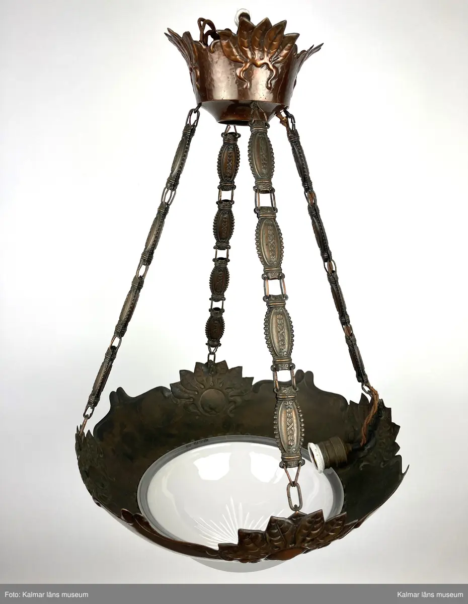 KLM 45619:396. Lampa, taklampa. Av metall med frostad vit glaskupa liggande på metallstommen. Glaskupan har slipat mönster från centrum likt en stjärna. Fyra kedjor som utgörs av avlånga metalldetaljer. Sockel för en glödlampa vid sidan av stommen samt överst i metallkupan upp mot taket.