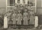Gruppfoto av sjuksköterskor och två män i uniform m/1939 på en trappa.