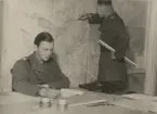 Löjtnant vid luftvärnet läser vid skrivbord, en annan står vid en väggkarta, uniform m/1939.