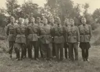 Infanterister uppställda på gräsplätt framför skog, uniform m/1939.