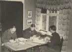 Tre män, varav en kavallerist, arbetar vid bord, uniform m/1939.