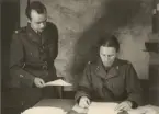 Kavallerist läser vid skrivbord, en infanterilöjtnant räcker honom ett papper, expeditionstjänst, uniform m/1939.