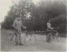 Två sjukvårdare med bår mellan cyklar vid landsväg. Uniform m/1910.