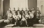 Volontärernas höstbal. Nio unga soldater i uniform m/1910 uppställda i en salong bakom sittande kvinnor.