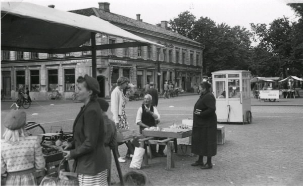 Torghandel på Varbergs torg med vy mot Lundquistska huset i kv Brunnsparken. På hörnan ligger Järnaffär Carl Nilsson & Son. Närmast ett par grönsakshandlare som bl a saluför blomkål. I kioskerna längre bort säljs glass; den bortre för Trollhätteglass.