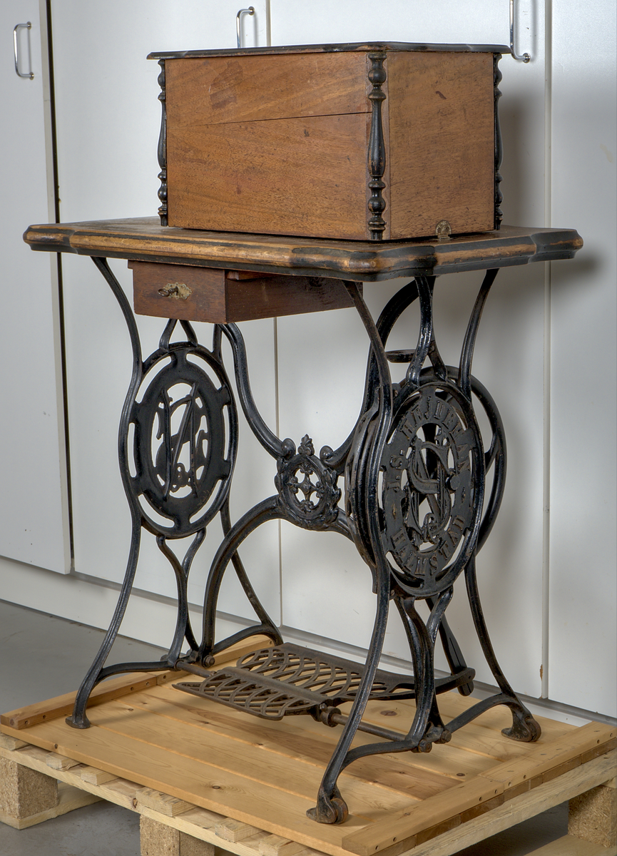 Trampsymaskin med dekorativt gjutjärnsunderrede och en träskiva som arbetsyta.

Svartmålad maskin dekorerad med sirlig ornamentik i guldfärg. På maskinens framsida sitter två märkta plåtar:

1. En referenstabell, för nålar?
2. Signering: "J.S. Hejdeman, Halmstad. Symaskin försäljning".

Maskinen är monterad på en profilerad träskiva av ek, försedd med en måttstock i intarsia på skivans framsida. Under bordet finns en skjutbar tillbehörslåda med låsmekanism. Maskinen skyddas av en rektangulär huv av ek, försedd med fyra dekorativa, svarvade hörnstolpar.

Det svartlackerade gjutjärnsstativet har en dekorativ utformning. På var sida av stativet finns två ovala medaljonger med relieftexten: "J.S. HEJDEMAN, HALMSTAD". De båda benen på höger sida av ställningen är försedda med hjul.