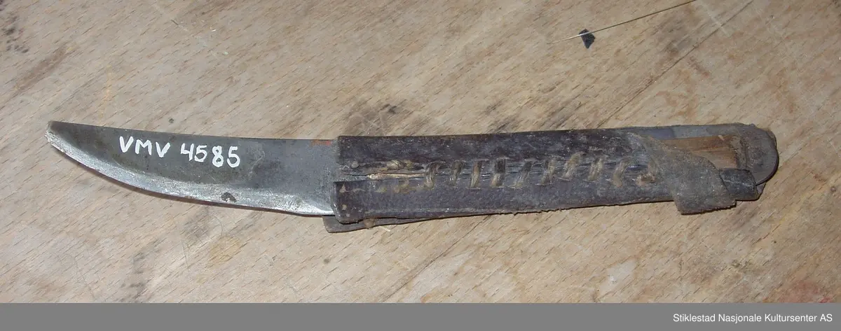 Krum skomakerkniv med påsydd hylse av skinn. Under skinnet ligger ett lite trestykke av nåltre. Skinnet er revnet i bakre ende av kniven.