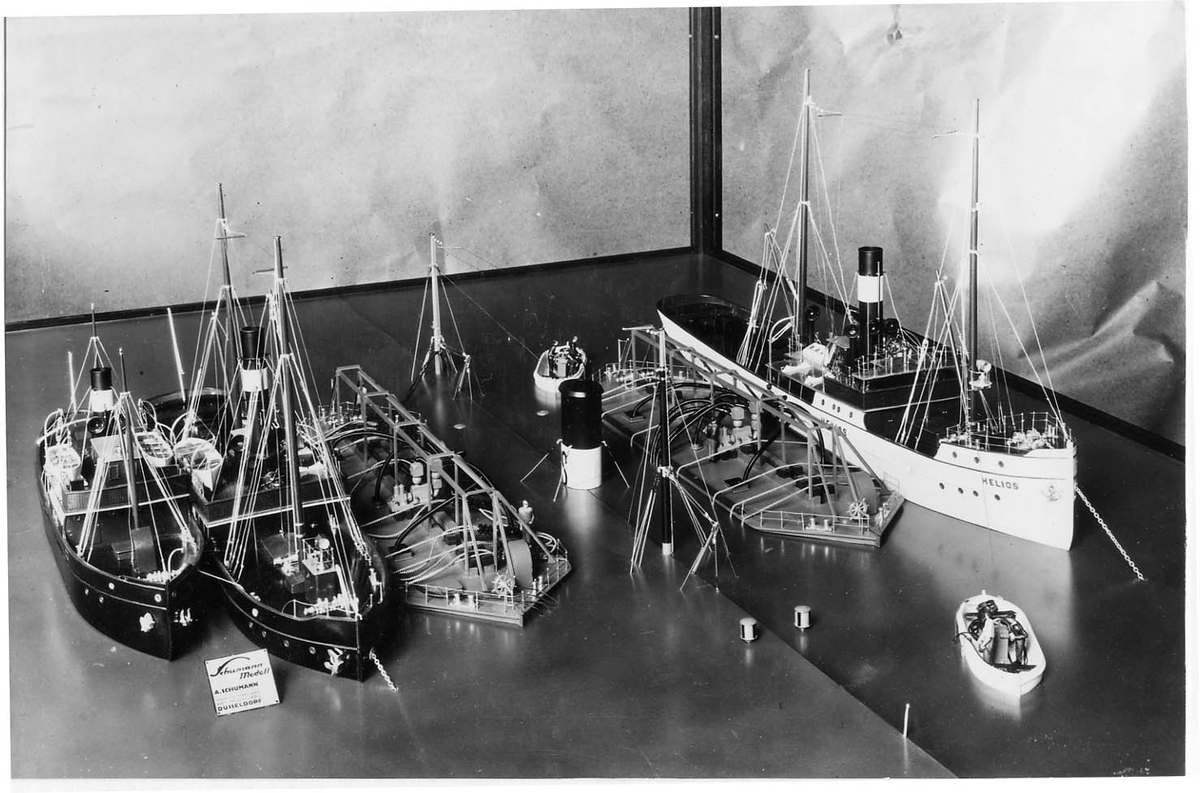 Modell i monter visande bärgningen av den förlista passagerarångaren HEIMDALL vid Ryssmasterna i Stockholms skärgård i oktober 1929. Närmast vraket Neptunbolagets bärgningspontoner ODEN och FRIGG.